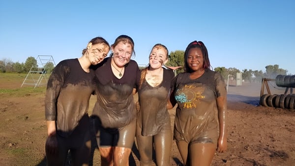 Un grupo de cuatro estudiantes se encuentra en un campo bajo un cielo azul y árboles en el terreno de la Toormina High School.
