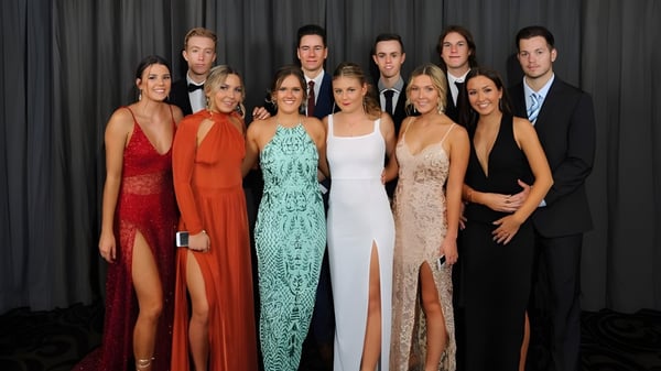 Un grupo de personas en ropa formal posan juntos frente a un fondo oscuro en el campus de la Toormina High School.