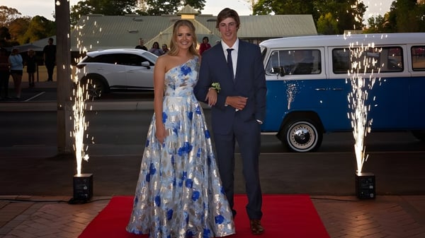 Una pareja en ropa formal está sobre la alfombra roja frente a una vieja furgoneta azul en el campus de la Toowoomba Anglican School.