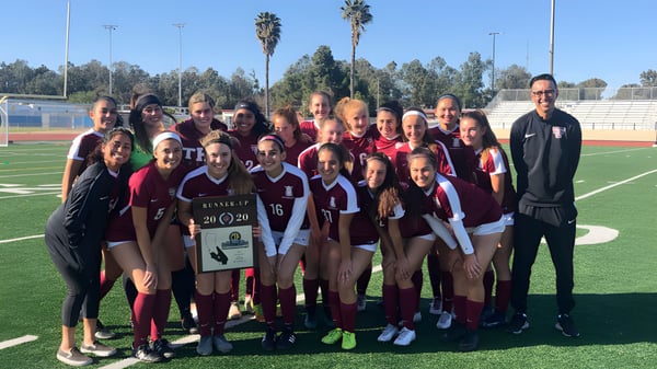 Un grupo de jóvenes futbolistas y su entrenador están juntos en el campo de fútbol del Torrance Unified School District.