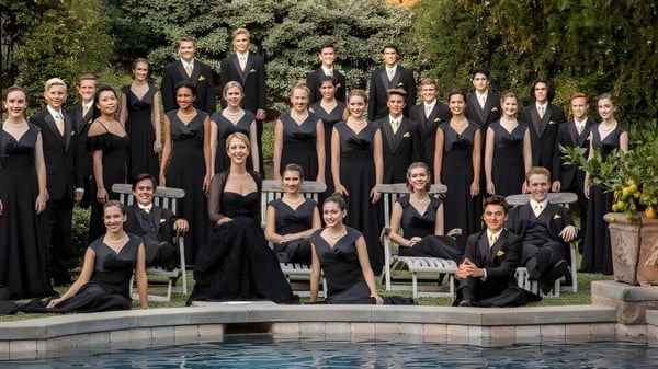Un grupo de estudiantes de la Trafalgar Castle School está de pie en ropa formal negra junto a una piscina al aire libre con un entorno verde.