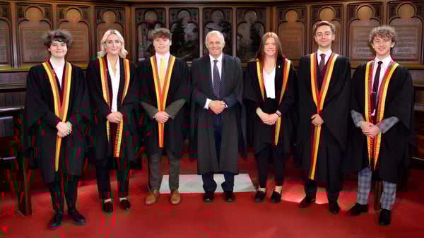 Un grupo de personas en togas académicas está en una ceremonia de graduación en el campus del Trent College.
