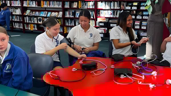 Estudiantes de la Trident High School examinan equipos y materiales médicos en un aula con estanterías.