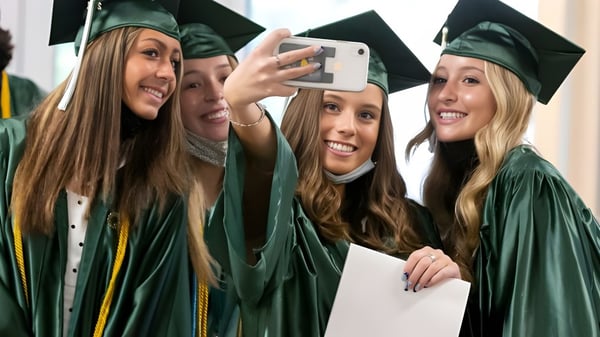 Cuatro estudiantes de la Trinity Bay State High School se toman un selfie juntas en togas de graduación verdes después de la ceremonia de graduación.