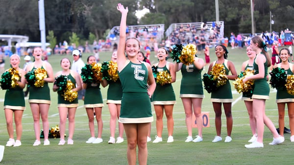 Porristas en uniformes verdes con pompones dorados están en el campo deportivo de la Trinity Catholic High School.