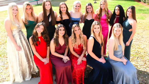 Un grupo de estudiantes de la Trinity Catholic High School posan en un prado frente a un edificio de ladrillo.