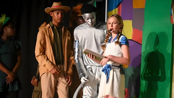 Alumnos de la Trinity Christian Academy posan con coloridos trajes de teatro frente a un fondo abstracto colorido.