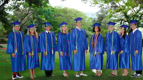 Un grupo de graduados de la Trinity Christian School está de pie en togas azules en el área exterior verde.