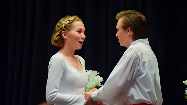Una joven pareja está de pie en ropa formal en el escenario de la Trinity Christian School frente a un telón oscuro.