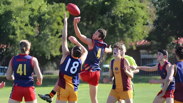 Alumnos del Trinity College juegan al fútbol australiano en un campo de hierba con un entorno verde.