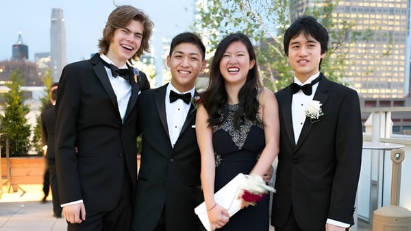 Cuatro estudiantes de la Trinity School posan frente a un paisaje urbano con altos edificios.