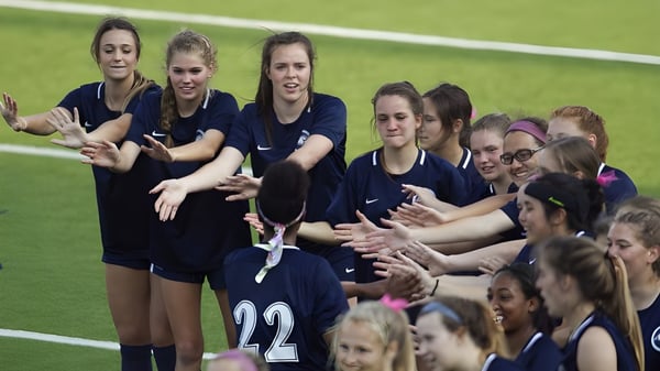 Un grupo de jugadoras de fútbol de la Trinity School celebra juntas en el campo de césped.