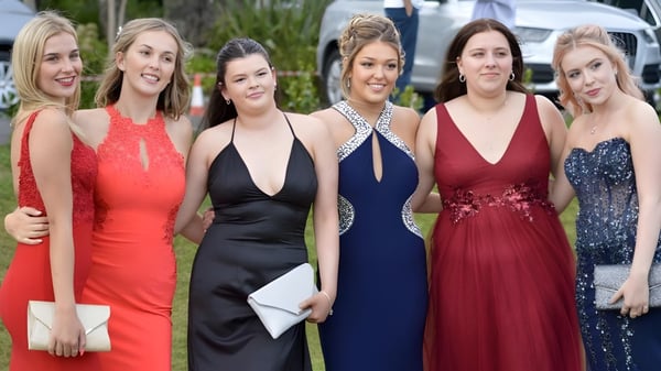 Seis alumnas de la Truro High School for Girls posan en elegantes vestidos de noche juntas al aire libre frente a un fondo verde.