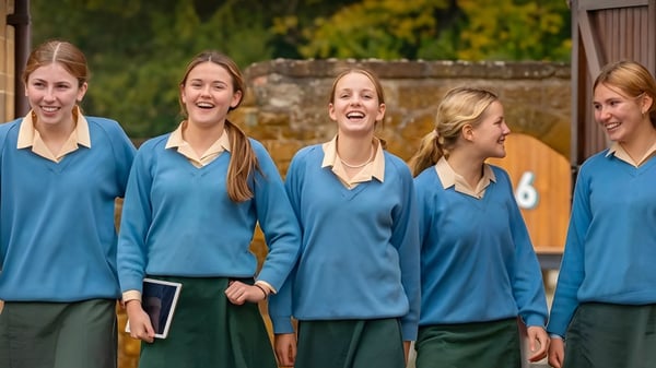 Un grupo de cinco estudiantes de Tudor Hall School está de pie en otoño frente a hojas otoñales y conversando.