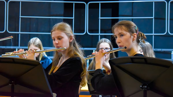 Dos estudiantes de Tudor Hall School tocan la flauta en el escenario frente a un fondo oscuro con iluminación.
