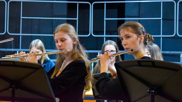 Dos estudiantes de Tudor Hall School tocan la flauta en un escenario con fondo oscuro.