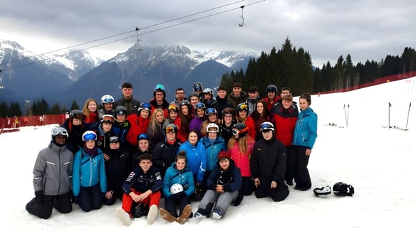Un grupo de estudiantes del Tullamore College está vestido con coloridos trajes de invierno en un paisaje montañoso nevado.