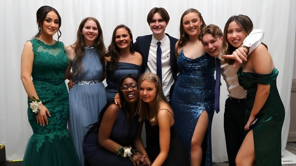 Un grupo de personas vestidas elegantemente posan juntas frente a un fondo blanco en el campus del Tyndall College.