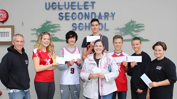 Estudiantes y personal de la Ucluelet Secondary School posan juntos frente a un pasillo escolar y muestran certificados.