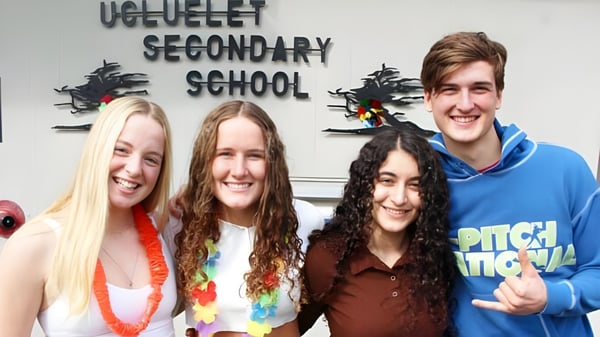 Cuatro estudiantes sonríen frente a un cartel de la Ucluelet Secondary School.