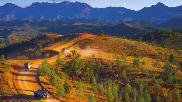 Una carretera de grava sinuosa atraviesa un paisaje montañoso con colinas coloridas y poderosas montañas a lo lejos cerca de la Underdale High School.