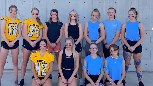 Un grupo de jóvenes deportistas posan juntas frente a una cerca de madera en el terreno de la Union High School.