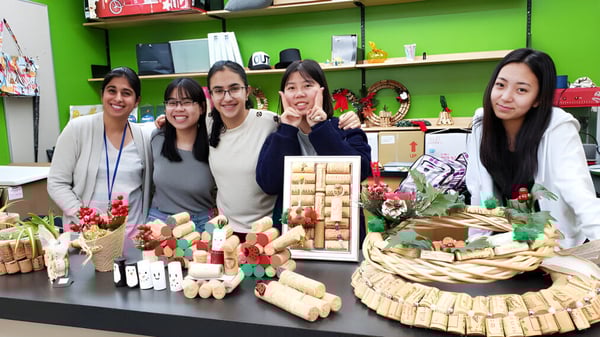 Un grupo de estudiantes de la University Hill Secondary School está detrás de una mesa con varias manualidades navideñas en una habitación colorida.