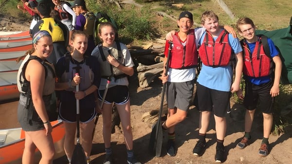 Un grupo de estudiantes de la University Lake School está de pie en ropa de senderismo en un camino en medio de la naturaleza verde.