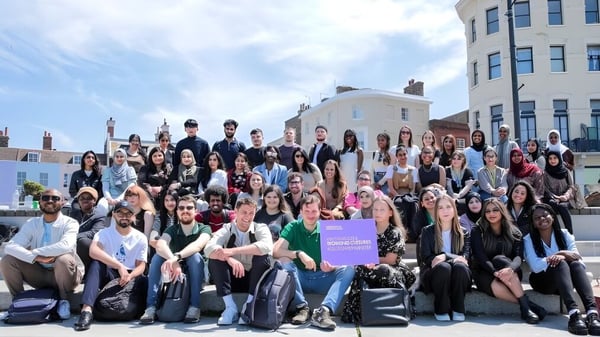 Un grupo de estudiantes se reúne frente a un edificio en el campus de la University of Westminster bajo un cielo azul.