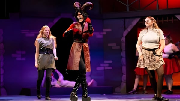 Estudiantes en coloridos disfraces realizan una actuación en el escenario de la University of Wisconsin-Superior frente a un fondo colorido.