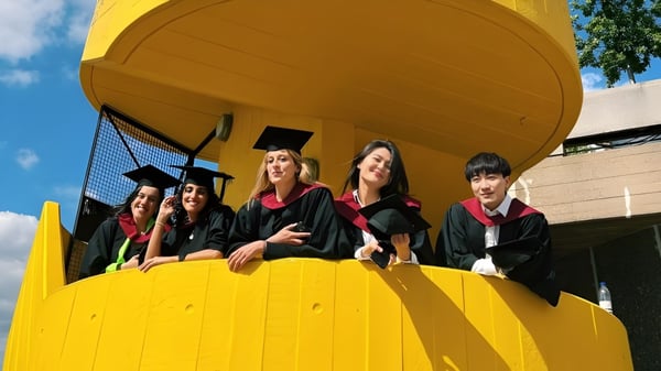 Un grupo de graduadas y graduados de la University of Westminster está en túnicas rojas frente a un edificio amarillo.