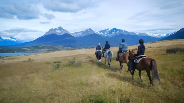 Estudiantes del Upper Canada College montan a caballo sobre un campo verde con montañas nevadas al fondo.