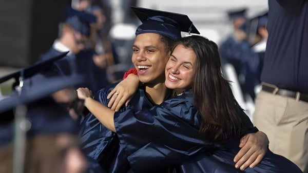 Dos graduados en togas azules se abrazan frente al Upper Coomera State College durante la ceremonia de graduación.