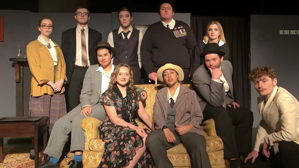 Un grupo de estudiantes del Upper Hutt College está de pie en ropa formal en el escenario con decorados de escenario al fondo.