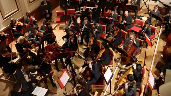 Un gran grupo de graduados de la Uppingham School se reúne en un magnífico salón para la ceremonia de graduación.