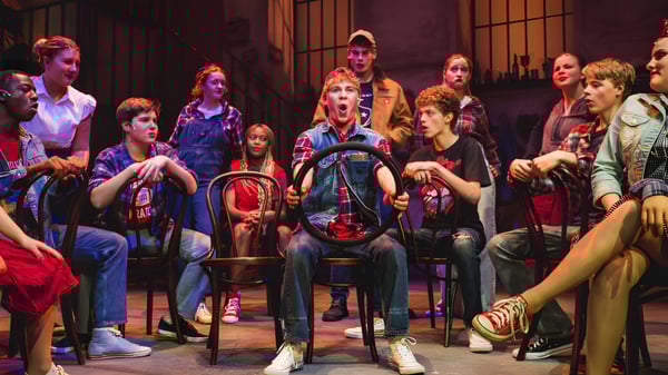 Un grupo de estudiantes de la Uppingham School se reúne en un escenario de teatro con poca luz y un fondo de escenario colorido.