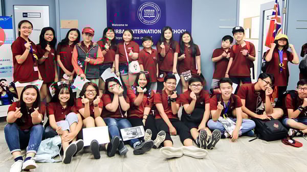 Un grupo de estudiantes en uniformes rojos posan frente a un fondo de AIESEC International en el campus de la Urban International High School.