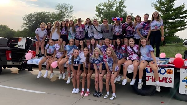Un grupo de alumnas del Urbandale Community School District posan frente a un vehículo al aire libre bajo un cielo despejado.