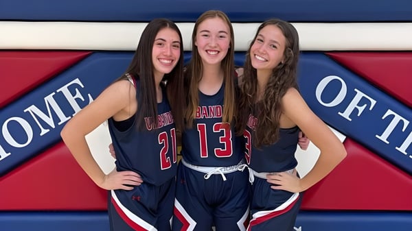 Tres estudiantes de Urbandale High School en uniformes deportivos posan juntas frente a un fondo colorido.