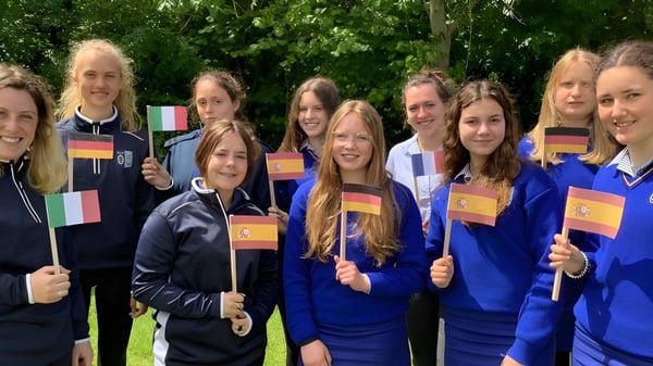 Estudiantes de la Ursuline Secondary School (Cork) están afuera en uniformes azules sosteniendo varias banderas de países.