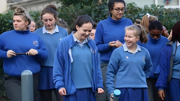 Un grupo de estudiantes de la Ursuline Secondary School en Cork está al aire libre frente a árboles y edificios.