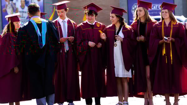 Graduados de la Utah Prep Academy en togas rojas y negras están juntos frente a un fondo de ciudad desenfocado.