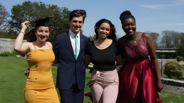 Cuatro personas están juntas al aire libre en el campus del UWC Atlantic College con árboles y un cielo despejado de fondo.