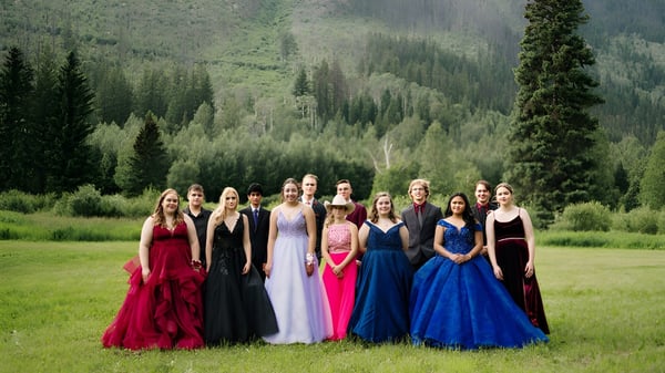 Un grupo de jóvenes estudiantes en vestidos coloridos está junto en el paisaje montañoso boscoso en el terreno de la Valemount Secondary School.