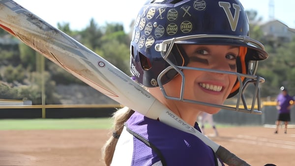 Una joven jugadora de softball está en el campo de béisbol de la Valencia High School con un bosque de fondo.