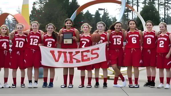 Un grupo de jóvenes atletas de la Valley View Secondary sostiene un banner de Vikes frente a un arco colorido al aire libre.