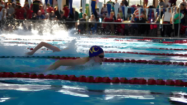 Una nadadora con gorra de baño azul y gafas de natación compitiendo en la piscina del Vancouver Community College.