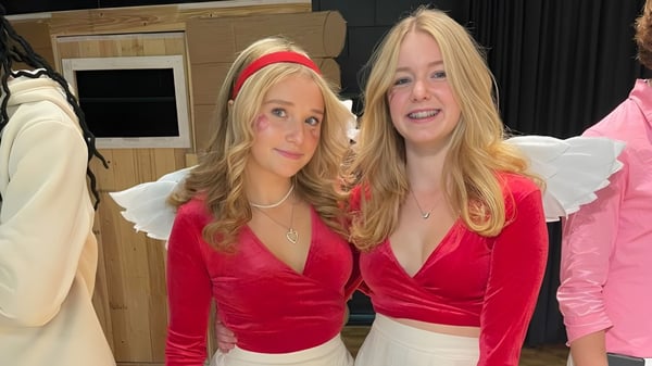 Dos estudiantes del Vankleek Hill Collegiate Institute llevan blusas de terciopelo rojas y están de pie frente a estantes de ropa y una estructura de madera.