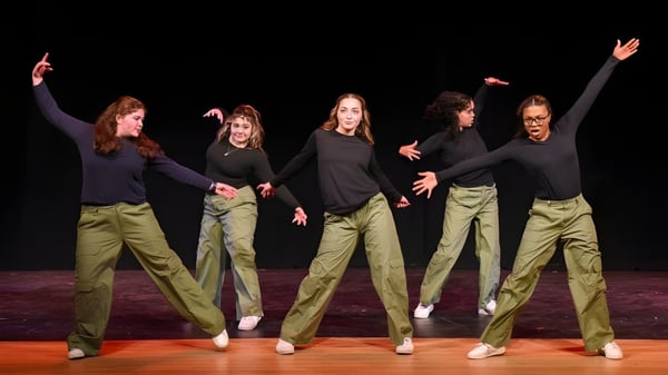 Un grupo de cinco estudiantes de la Vermont Academy realiza una actuación de baile sincronizado en un escenario con fondo oscuro.