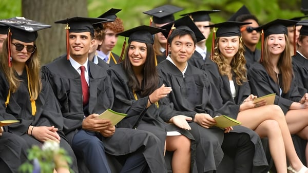 Un grupo de graduados de la Vermont Academy está sentado con ropa académica al aire libre frente a unos árboles.